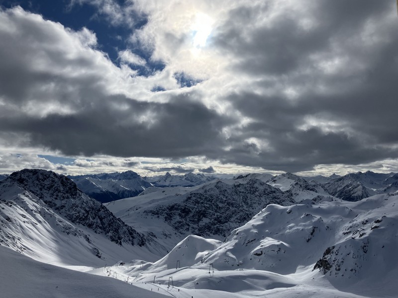01 (Titelbild): Weitläufiges Bergpanorama mit Sonne, die Berge und Wolken beleuchtet und ein eindrucksvolles Licht- und Schattenspiel erzeugt.